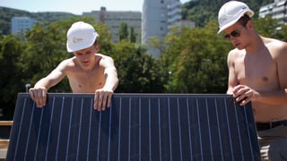 Lehrlinge montieren Solarzellen auf einem Dach.