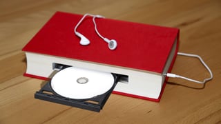 Ein rotes Buch, das gleichzeitig ein CD-Laufwerk ist, daran angeschlossen ein Kopfhörer.