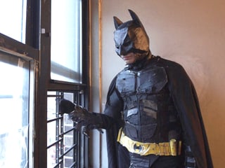 Eine verkleidete Batman-Figur am Fenster, hinausschauend.