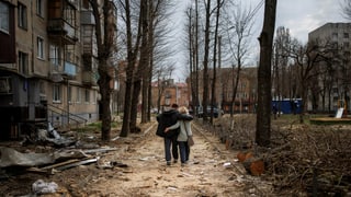 Mann und Frau umarmen sich und laufen gleichzeitig in Trümmern eine Strasse runter, Aufnahme von hinten. Sie laufen also weg. 