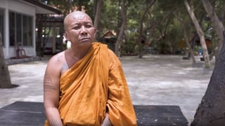 Buddhistischer Mönch sitzt auf einer Bank in seiner Tempelanlage.