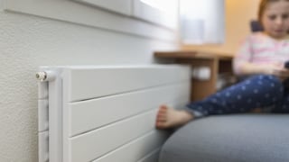 Mädchen im Hintergrund wärmt ihre Füsse an einem Heizkörper Mädchen im Hintergrund wärmt ihre Füsse an einem Heizkörper