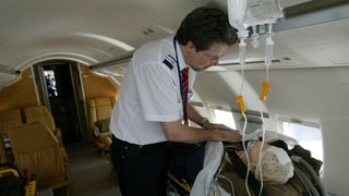 Ein Arzt betreut einen mit einer Puppe simulierten Patienten in einem Jet.