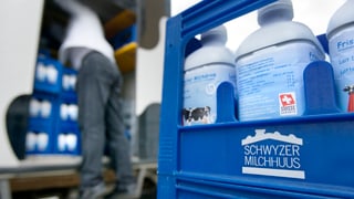 Milch in Harassen, im Hintergrund ein Mann der sie aus einem Lastwagen auslädt.