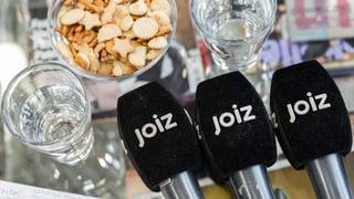 «Joiz»-Mikrofone auf einem Glastisch mit Apero-Gebäck und Wassergläsern.