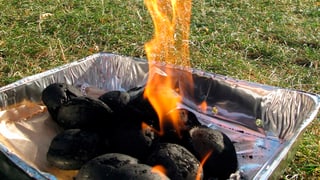 Ein Einweggrill wird auf einer Wiese angeglüht