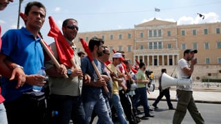 Auf einer Linie marschierende Demonstranten mit roten Fahnen.