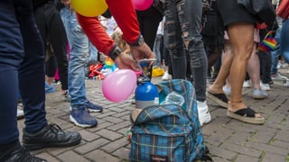 Eine Person füllt einen Ballon aus einer kleinen Gasflasche in einem Rucksack am Boden.