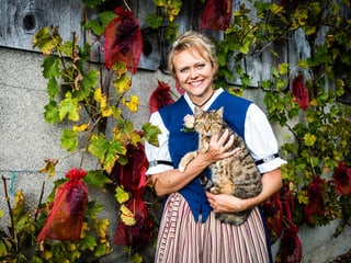 Brigitte steht vor einer rebenbewachsenen Mauer. Sie hält eine Tiger-Katze im Arm.