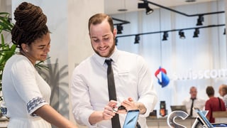 Zwei Swisscom-Angestellte sehen lächeln ein Mobiltelefon an