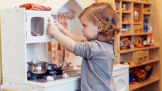 Ein Mädchen spielt mit einer Spielzeug-Kochnische.