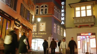 An einer Gasse in der Zürcher Altstadt steht das Kino Stüssihof. Es ist dunkel und die Leuchtschrift ist zu sehen.