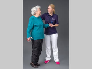 Seniorin steht auf den Zehenspitzen und wird von einer jungen Frau gestützt