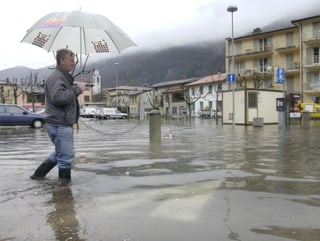 Mensch mit Schirm überquert einen überfluteten Parkplatz