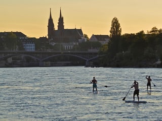 Stand Up Paddler auf dem Rhein mit dem Basler Münster im Hintergrund.