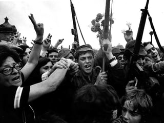 Schwarz-weiss-Bild von Soldaten und Bürgern, die mit Gewehren und Blumen auf der Strasse feiern.