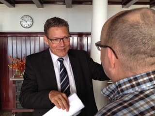 Mann in Krawatte, dahinter eine Uhr