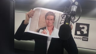 Mario Torriani hält sich ein Foto von Vujo vors Gesicht und post neben dem Mikrofon im SRF 3-Studio