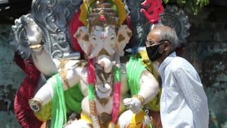 Ein Mann mit Maske vor einer Ganesha-Figur.