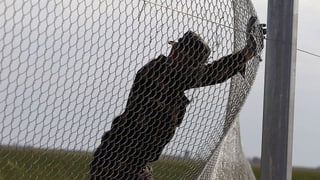 Ein Flüchtling drückt einen Zaun ein.