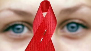 Eine Person hält das Symbol für die Aidsbekämpfung, eine rote Schlaufe, vor ihr Gesicht. Eine Person hält das Symbol für die Aidsbekämpfung, eine rote Schlaufe, vor ihr Gesicht.