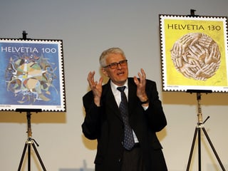 Ein Mann im Anzug stellt zwei Briefmarken vor.