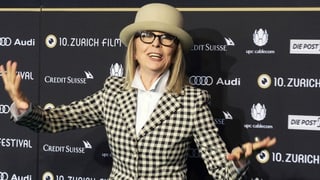 Frau mit kariertem Jacket und Hut und Hornbrille vor der Fotowand des Zurich Film Festivals.