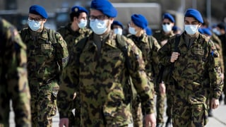 Soldaten mit Gesichtsschutz und blauen Berets in einer grossen Gruppe abgebildet.