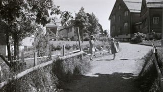 eine schwarz-weiss Fotografie von zwei Kindern inmitten Häusern und Garten