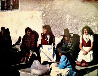 Frauen mit traditionellen bolivianischen Gewändern sitzen auf der Strasse. Mittendrin: Zwei Frauen in Frauen mit traditionellen bolivianischen Gewändern sitzen auf der Strasse. Mittendrin: Zwei Frauen in