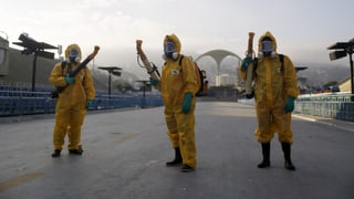 Drei Männer in gelben Schutzanzügen mit je einem Rohr zum Versprühen im Anschlag.