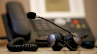 Ein Festnetztelefon, davor liegt ein Headset mit Kopfhörer und Mikrofon.