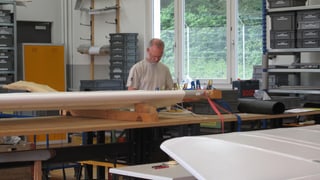 Ein Mann mit weissem T-Shirt arbeitet in einer Werkstatt an grossen weissen Flugzeugteilen. 
