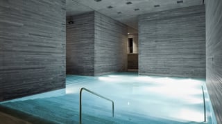 Schlichtes Thermalbad mit grauen Steinwänden und beleuchtetem Schwimmbecken