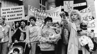 Brunner mit einer schwarzen Puppe im Arm inmitten von Demonstrantinnen, die mehr Frauen im Parlament fordern. Brunner mit einer schwarzen Puppe im Arm inmitten von Demonstrantinnen, die mehr Frauen im Parlament fordern.