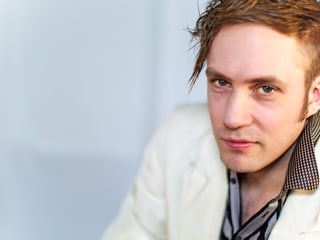 Johannes Kreidler in weissem Jackett blickt in die Kamera.