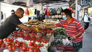 Ein Kunde mit Hygienemaske kauft Gemüse an einem Markt in London.