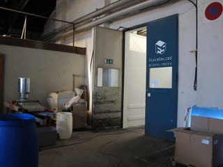 Eingangstüre mit dem Logo von FluidSolids, Grosse Plastikkübel, Gerätschaften und Kartonschachteln stehen herum.