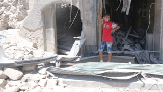Ein Junge mit rotem T-shirt steht in einer Öffnung eines zerstörten Gebäudes.
