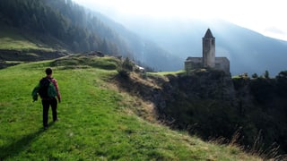Ein Mann spaziert über eine Wiese, im Hintergrund sieht man einen Wald und eine Kapelle. Ein Mann spaziert über eine Wiese, im Hintergrund sieht man einen Wald und eine Kapelle.