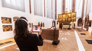 Frau betrachtet ein Kirchenschiff und hält dabei ein Tablet hoch. 