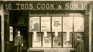 Ein Reisebüro mit der Aufschrift Thos. Cook & Son, eine Person steht in Türe, eine andere vor dem Schaufenster.