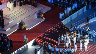 Papst auf Tribüne. Mehrere Personen tragen ein Kreuz.