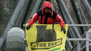 Eine Aktivistin montiert in luftiger Höhe ein gelbes Transparent mit der Aufschrift «The End». 