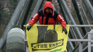 Eine Aktivistin montiert in luftiger Höhe ein gelbes Transparent mit der Aufschrift «The End». Eine Aktivistin montiert in luftiger Höhe ein gelbes Transparent mit der Aufschrift «The End».