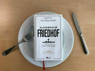 Das Buch «Die letzten Meter bis zum Friedhof» von Antti Tuomainen liegt auf einem weissen Teller. Messer und Gabel liegen hingeworfen daneben. Das Buch «Die letzten Meter bis zum Friedhof» von Antti Tuomainen liegt auf einem weissen Teller. Messer und Gabel liegen hingeworfen daneben.