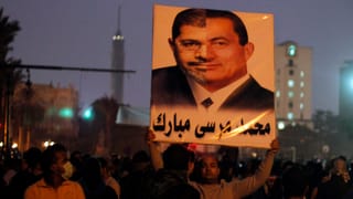 Ein Mann hält ein Plakat, auf dem je eine Gesichtshälfte von Mursi und von Mubarak zu sehen ist