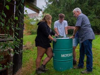 Drei Menschen stehen um eine Tonne Drei Menschen stehen um eine Tonne