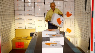 Ein Mitarbeiter von Zalando platziert zig weiss-orange Zalando-Pakete auf einem Förderband.
