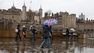 Symbolbild: Menschen vor dem London Tower, einer hat einen Regenschirm aufgespannt, der die britische Flagge zeigt.